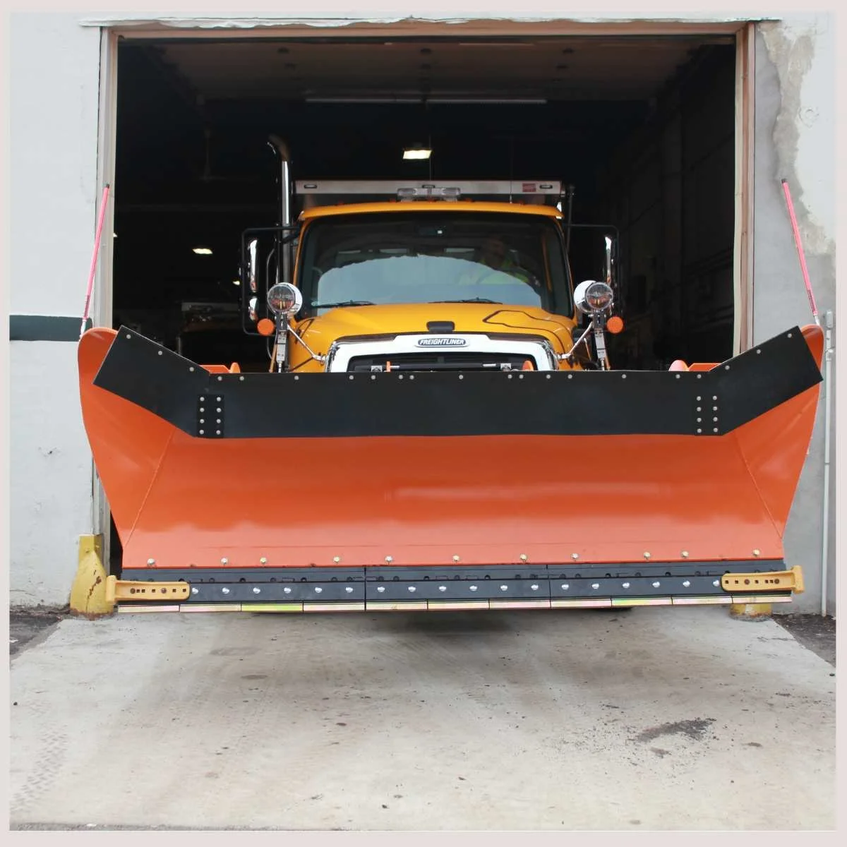 A large yellow snow plow stands ready for winter, showcasing its robust design and bright color against a snowy backdrop.