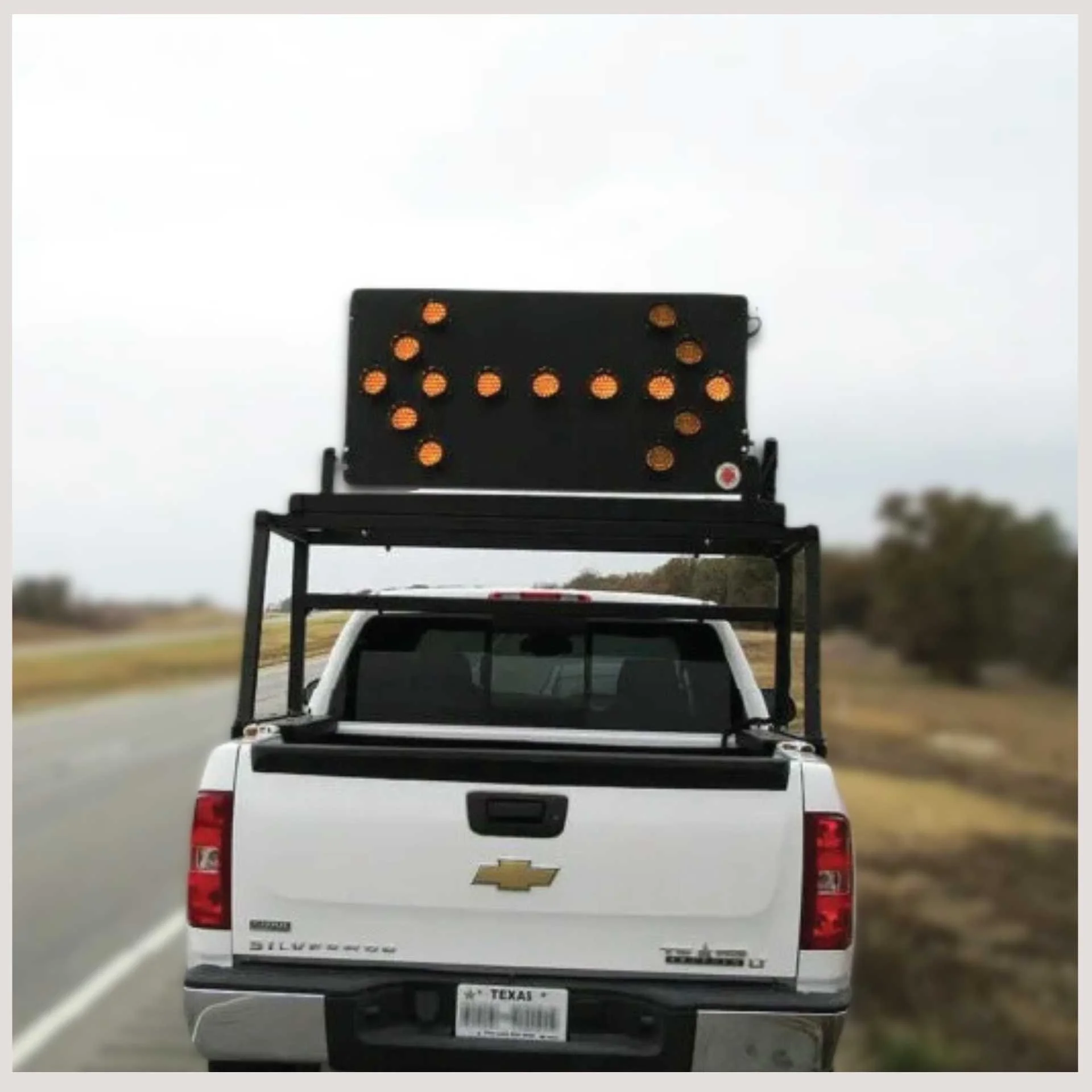 A truck displaying a sign on its rear, parked on a road with a clear blue sky in the background.
